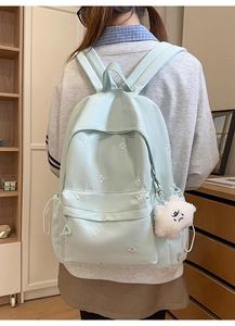 Detail of mint green school backpack with white clover embroidery and plush pendant