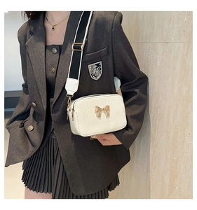 Close-up of a white textured crossbody bag featuring a golden bow buckle and contrast strap