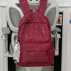Détail du sac à dos rouge avec motif étoiles et breloque en dentelle sur chaise