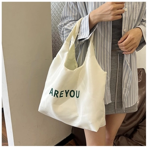 Gros plan sur un sac cabas en toile blanche avec texte vert porté par un mannequin chic