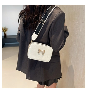 Detail of white wrinkled crossbody bag with golden bow and bicolor wide strap
