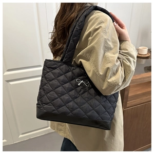Detailed view of quilted stitching and silver bow on black shoulder bag with smooth base