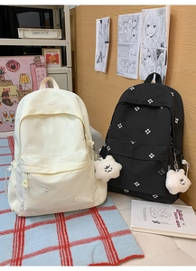 Detailed view of beige and black student backpacks with floral embroidery and cute plush charms