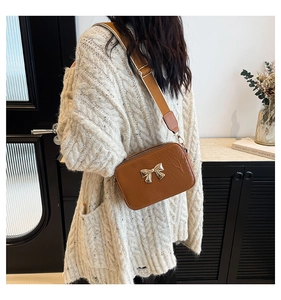 Detail view of brown PU leather crossbody bag with golden bow and adjustable strap