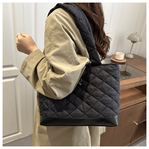 Detail of black quilted shoulder bag with leather patchwork and wide strap on model