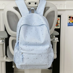 Détail d'un sac à dos bleu clair à motifs étoiles avec poches zippées sur une chaise blanche