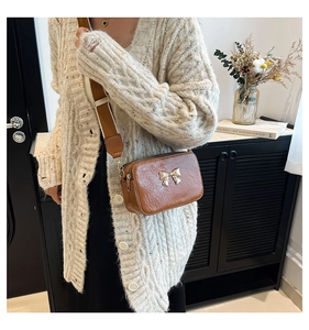 Brown crossbody bag with gold bow clasp and wide strap shown on a female model