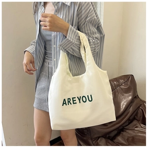 Détail d'un sac cabas en toile blanche avec lettres ARE YOU vertes porté par un mannequin