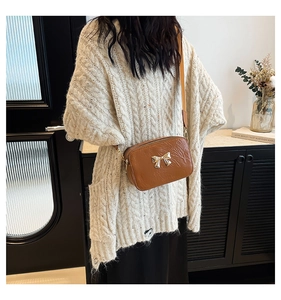 Close-up of brown crossbody bag with gold metal bow and wide strap on white sweater