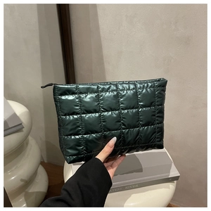 Detail of dark green quilted makeup bag with puffer texture and black zipper closure