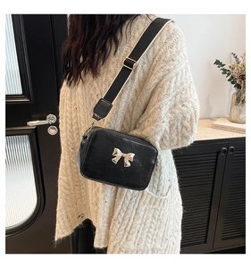 Close-up of black crossbody bag featuring a golden bow metal buckle and wide strap