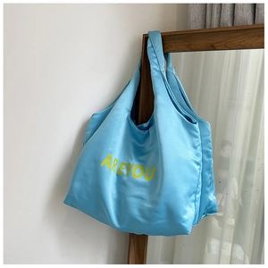 Détail d'un sac cabas en satin bleu avec lettres jaunes suspendu à un cadre en bois