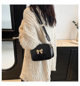 Detail of a black square bag featuring a gold bow buckle and textured embossed surface