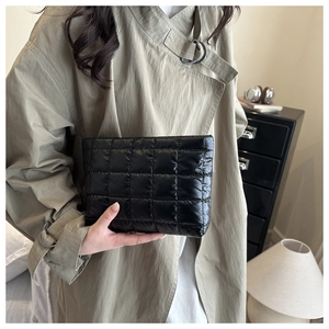 Quilted black clutch bag in puffy waterproof nylon material held by a model