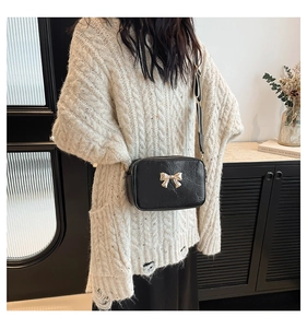 Detail of black crossbody bag with golden bow and adjustable wide shoulder strap