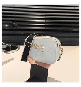 Detail of white textured crossbody bag with golden bow hardware and wide black strap