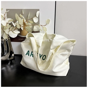 Détail d'un sac cabas blanc crème avec texte vert sur satin et accessoires élégants