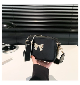 Detail of black crossbody bag with gold bow ornament and adjustable wide strap