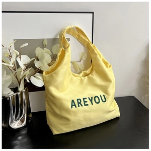 Détail d'un sac cabas en satin jaune vif avec lettres AREYOU imprimées en vert