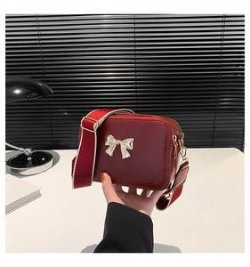 Detail of burgundy crossbody bag with golden bow hardware and wide contrast strap