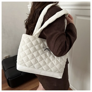Detail view of white quilted tote bag with rhombus stitching and small bow ornament