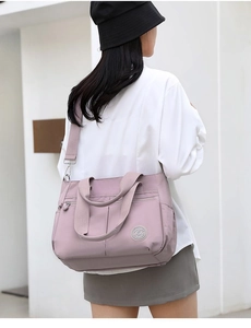 Detail of pink nylon multi-pocket tote bag showing the round logo and smooth zipper texture