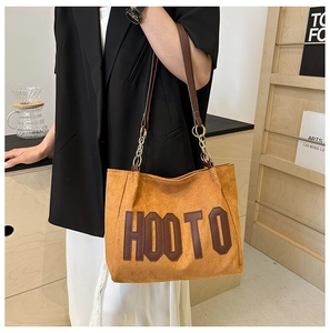 Détail du sac fourre-tout en daim marron avec lettrage HOOTO en cuir et chaîne en métal
