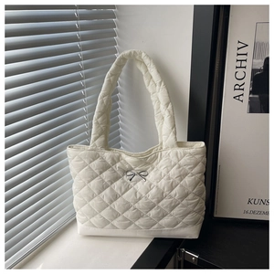 Close-up of white quilted tote bag featuring silver bow detail and rhombic stitching