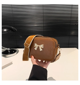 Detailed macro view of the golden metal bow accent and textured brown leather small square bag