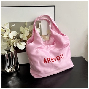 Détail d'un sac cabas en satin rose avec lettrage AREYOU rouge sur une table sombre