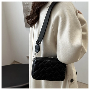 Detail of black quilted crossbody bag with wide strap on model in white coat