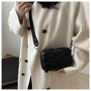 Detail of black quilted crossbody camera bag with wide strap and silver metal hardware