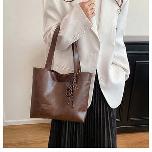 Detail view of large dark brown leather tote bag with a fashion tag and woven charm