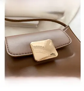 Close-up of brown leather bag featuring a large square golden buckle and fine stitching