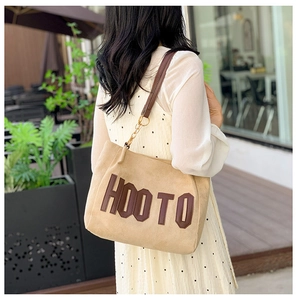 Sac fourre-tout en daim camel avec inscription HOO TO porté par un mannequin dans un café