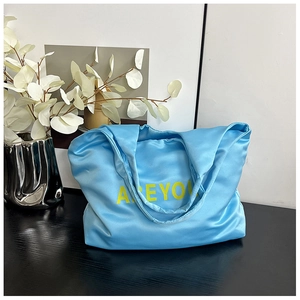 Détail du cabas en satin bleu avec imprimé AREYOU jaune sur une surface en bois