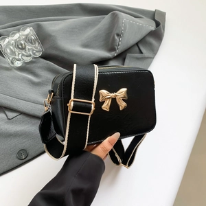 Classic black crossbody camera bag with golden bow accent and wide fabric shoulder strap