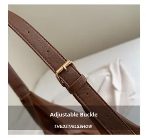 Detail view of the brown leather shoulder strap with adjustable golden pin buckle