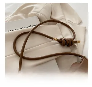 Detail of a brown leather shoulder bag featuring a knotted tubular strap and gold hardware