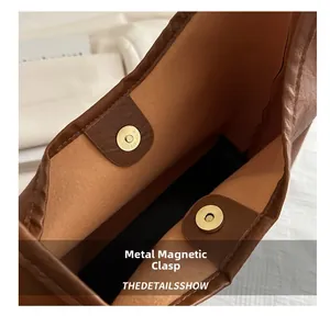 Detailed macro view of the magnetic metal closure on a brown leather bucket bag
