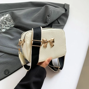 Creamy white pleated crossbody bag with gold bow ornament and wide fabric strap