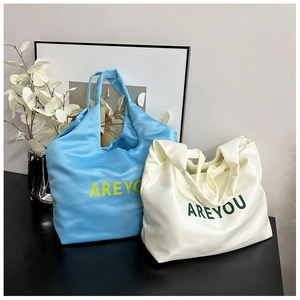 Détail de sacs cabas en soie bleu et beige avec inscription imprimée AREYOU