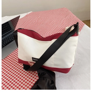 Detail view of canvas crossbody bag with burgundy trim and adjustable black strap