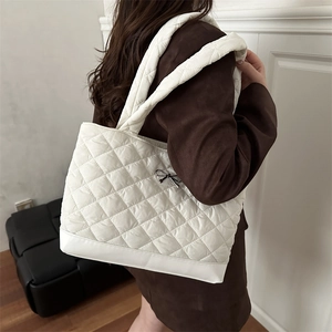 Chic white quilted tote bag with a metal bow detail and wide shoulder strap