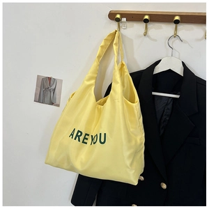Détail du sac cabas en nylon jaune avec lettrage ARE YOU vert suspendu à un crochet en bois