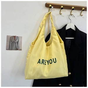 Détail du sac cabas en nylon jaune avec imprimé lettres vertes sur un crochet bois