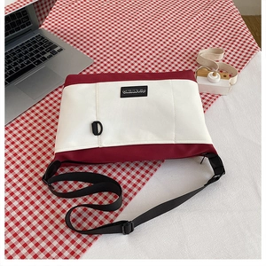 Detail of red and white canvas crossbody bag with black adjustable strap and brand label