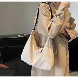 Détail d'un grand sac fourre-tout en toile crème avec bandoulière sur un trench-coat kaki