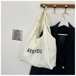 Détail du sac fourre-tout en toile crème avec lettrage AREYOU vert sur un crochet mural