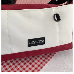 Detailed close-up of a red and white canvas messenger bag with a rubber brand logo